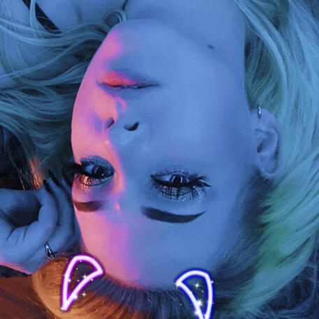 Image of Megan, with blue and pink lighting and fake devil horns. The entire image is flipped upside down.